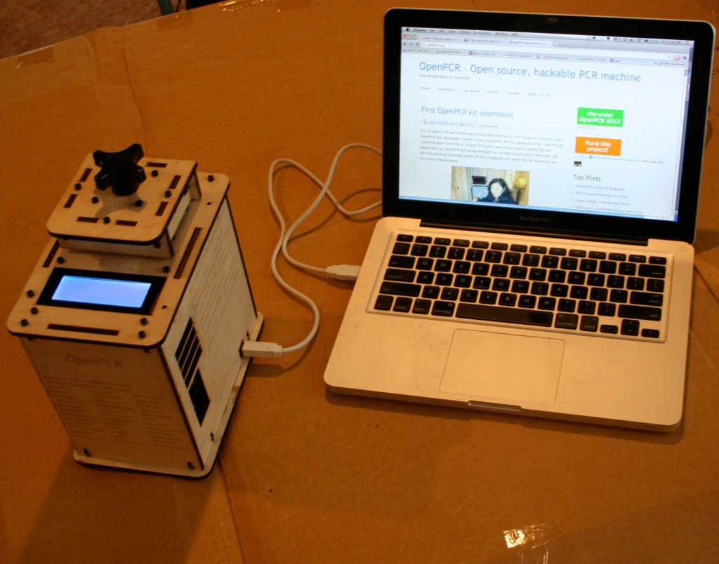 OpenPCR machine beside a laptop, displaying a webpage about the open-source PCR device.